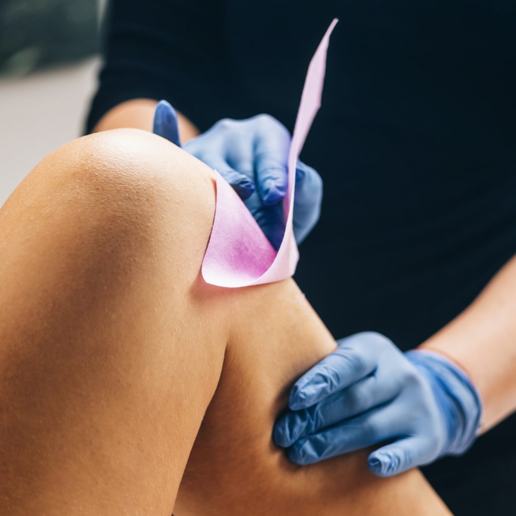 Waxing - Beautician Removing Unwanted Hair from Female Leg with hair removal Wax Strips
