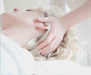 Blond haired woman lying down and receiving a wellness head and neck massage from a professional